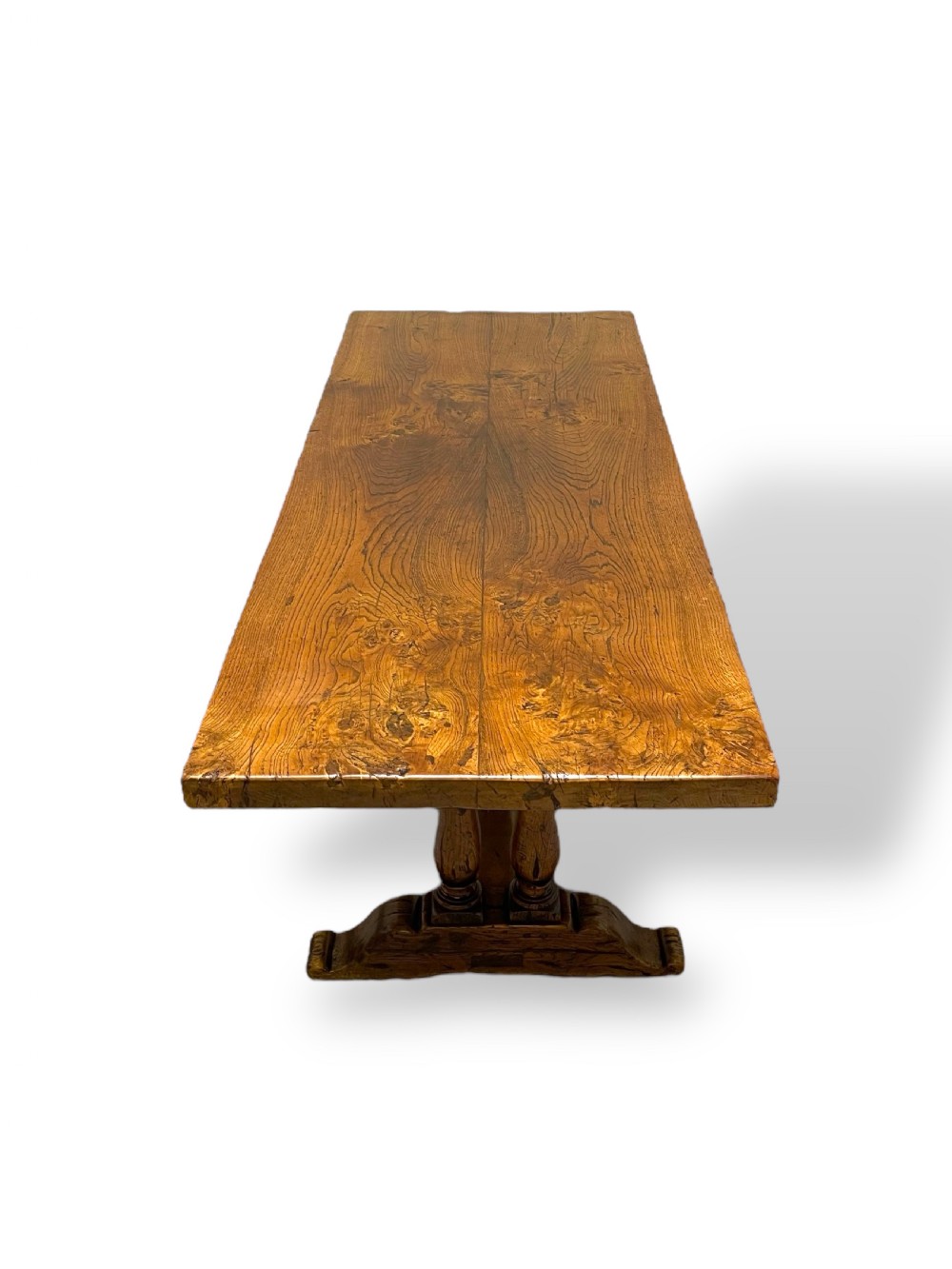 A solid warm brown oak refectory dining table featuring a thick rectangular top supported by double turned columns and a central stretcher. View VI