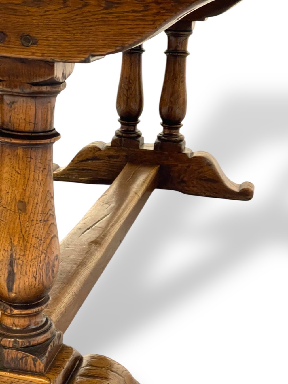 A solid warm brown oak refectory dining table featuring a thick rectangular top supported by double turned columns and a central stretcher. View IX