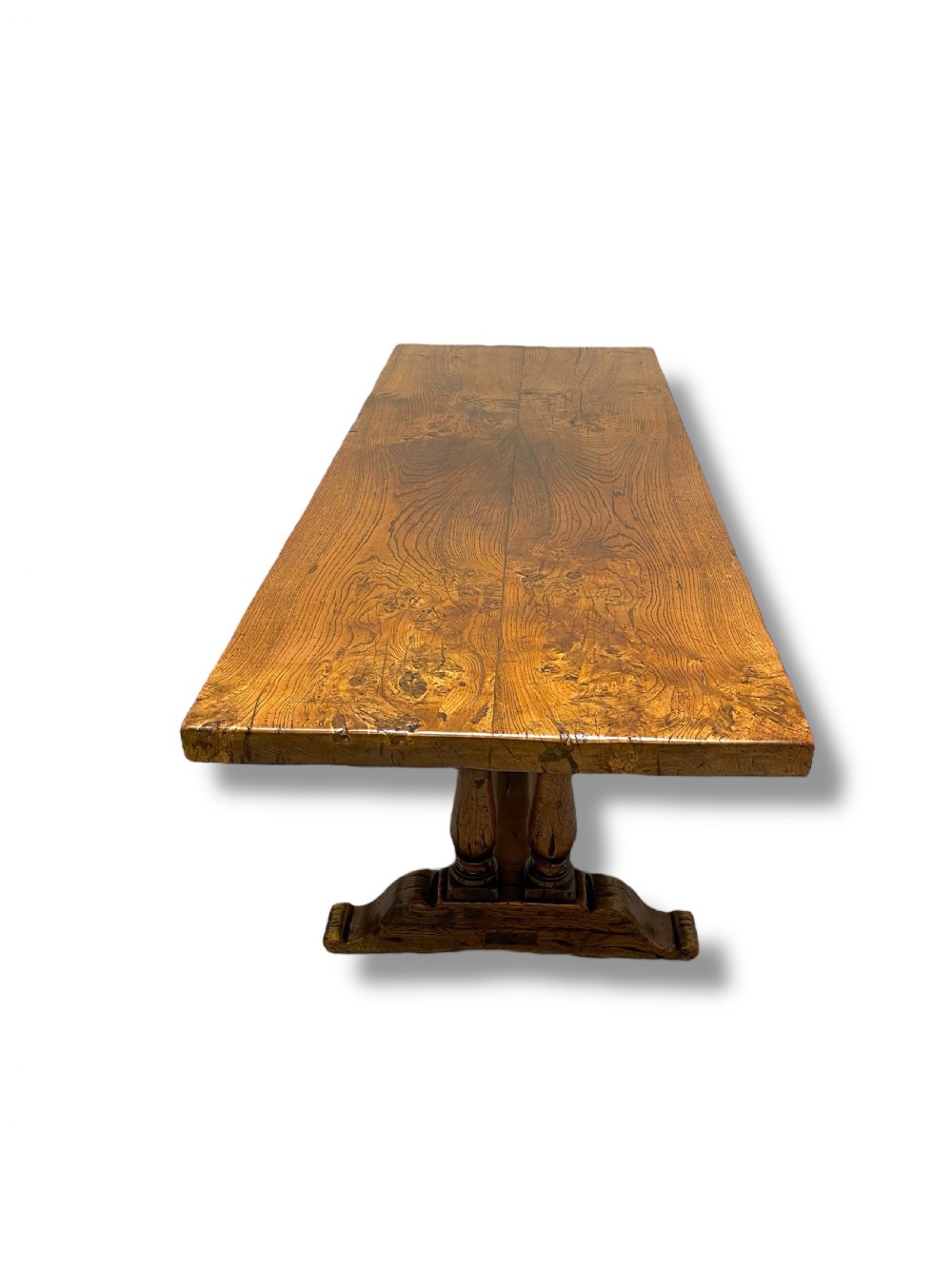 A solid warm brown oak refectory dining table featuring a thick rectangular top supported by double turned columns and a central stretcher. View X
