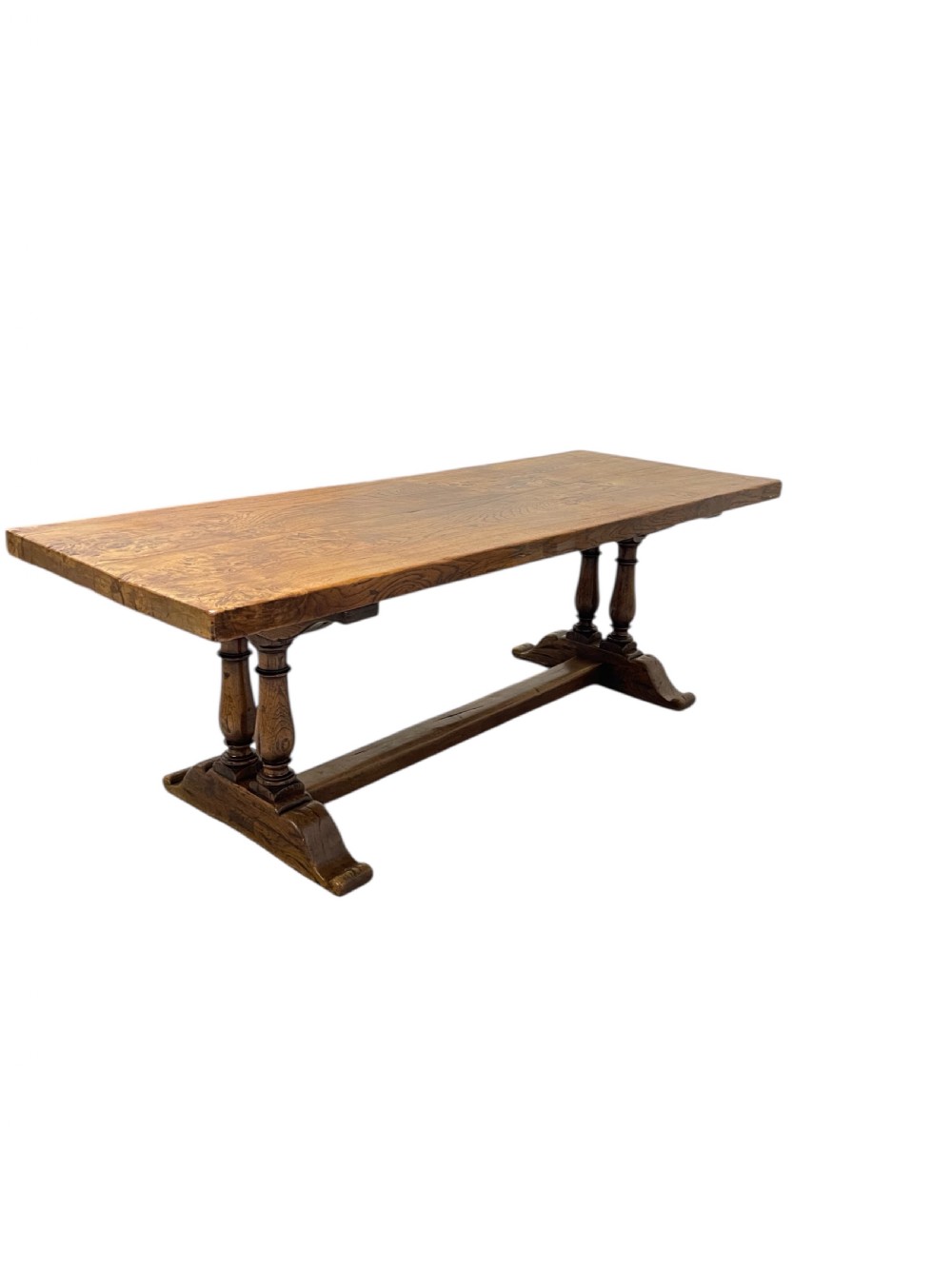 A solid warm brown oak refectory dining table featuring a thick rectangular top supported by double turned columns and a central stretcher. View XII
