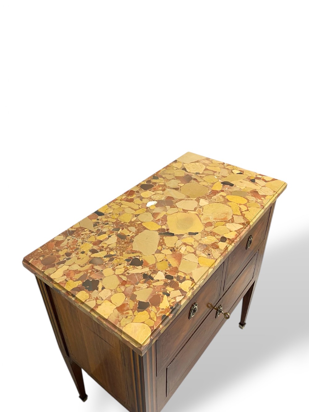 A Louis XVI style wooden commode featuring geometric parquetry inlay, a variegated marble top, three drawers with brass escutcheons, and tapered square legs. View VII