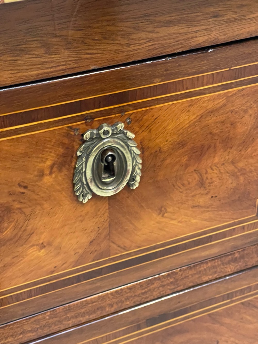 A Louis XVI style wooden commode featuring geometric parquetry inlay, a variegated marble top, three drawers with brass escutcheons, and tapered square legs. View IX