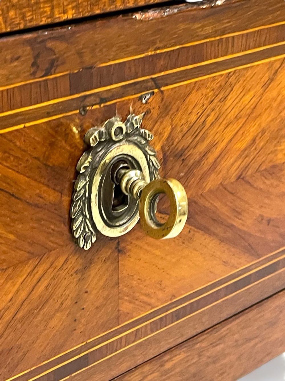 A Louis XVI style wooden commode featuring geometric parquetry inlay, a variegated marble top, three drawers with brass escutcheons, and tapered square legs. View X