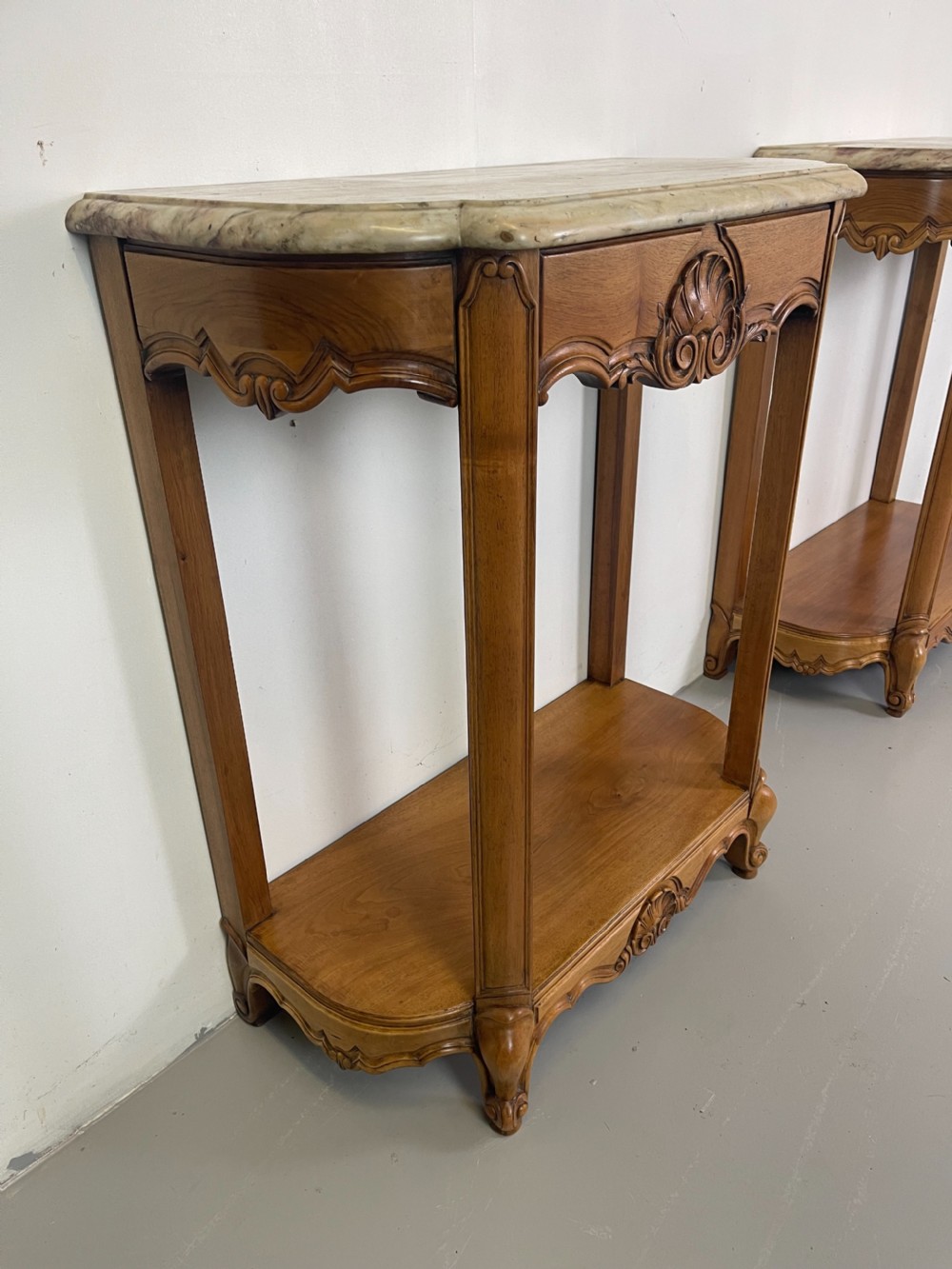 A pair of French Louis XV style walnut console tables featuring shaped marble tops, carved shell aprons, lower shelves, and cabriole legs. View V