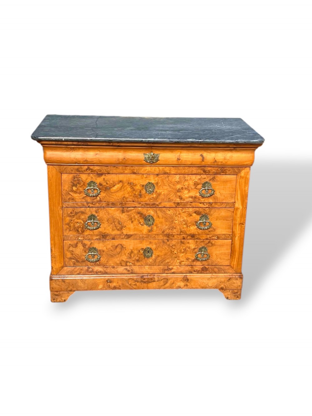 A French Louis Philippe style burr ash commode featuring a dark grey marble top, four drawers, and ornate brass handles.
