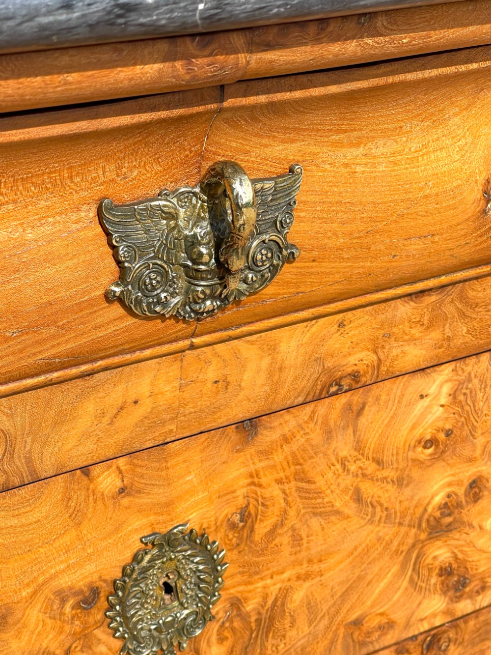 A French Louis Philippe style burr ash commode featuring a dark grey marble top, four drawers, and ornate brass handles. View III