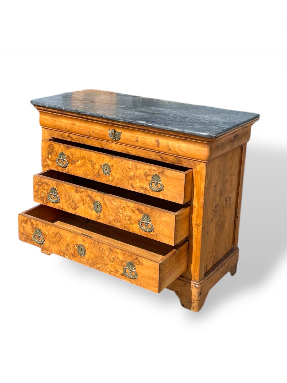 A French Louis Philippe style burr ash commode featuring a dark grey marble top, four drawers, and ornate brass handles. View X