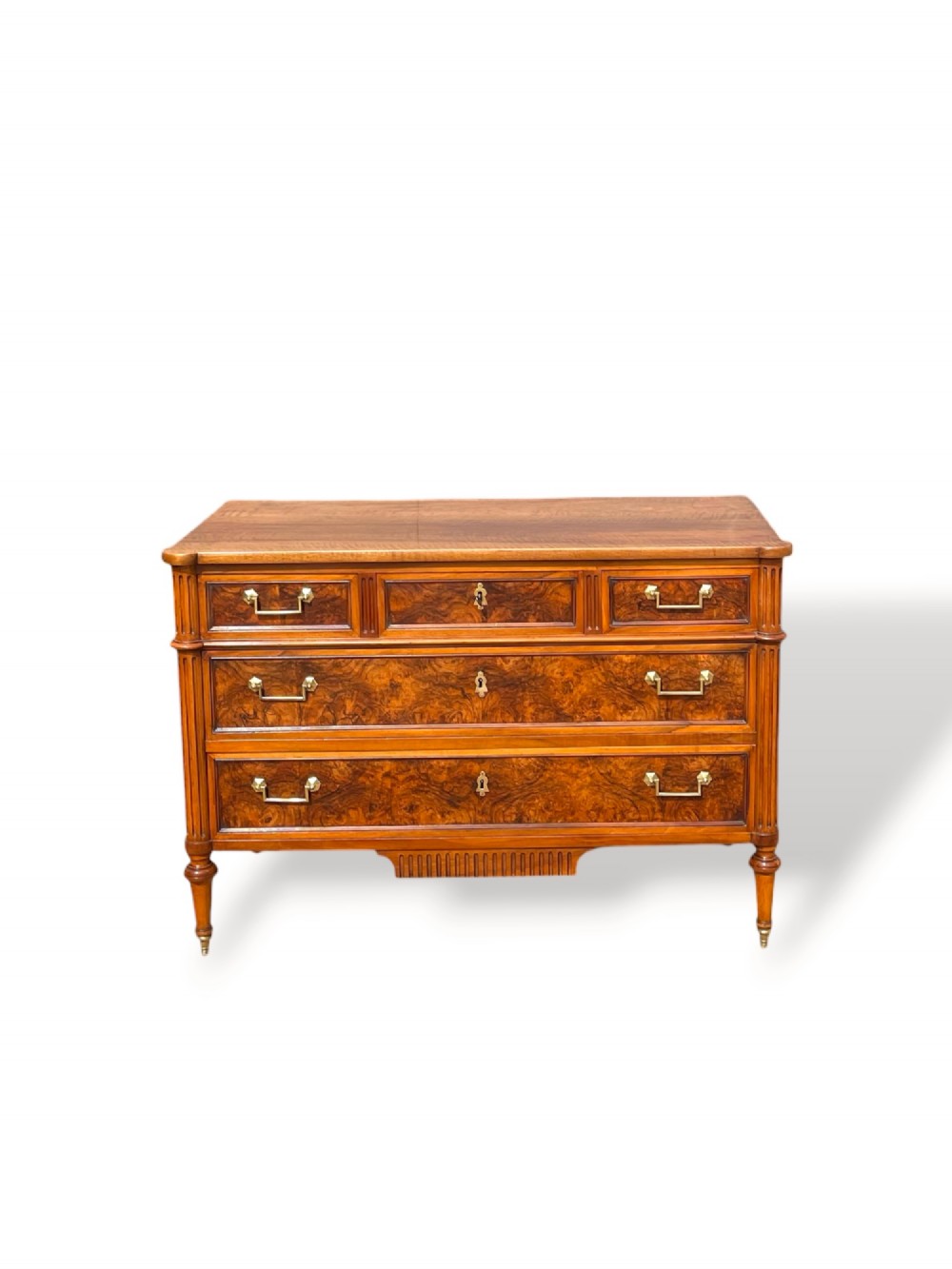 An eighteenth-century French walnut commode featuring figure-grained drawer fronts, brass handles, fluted corner pilasters, and tapered turned legs.