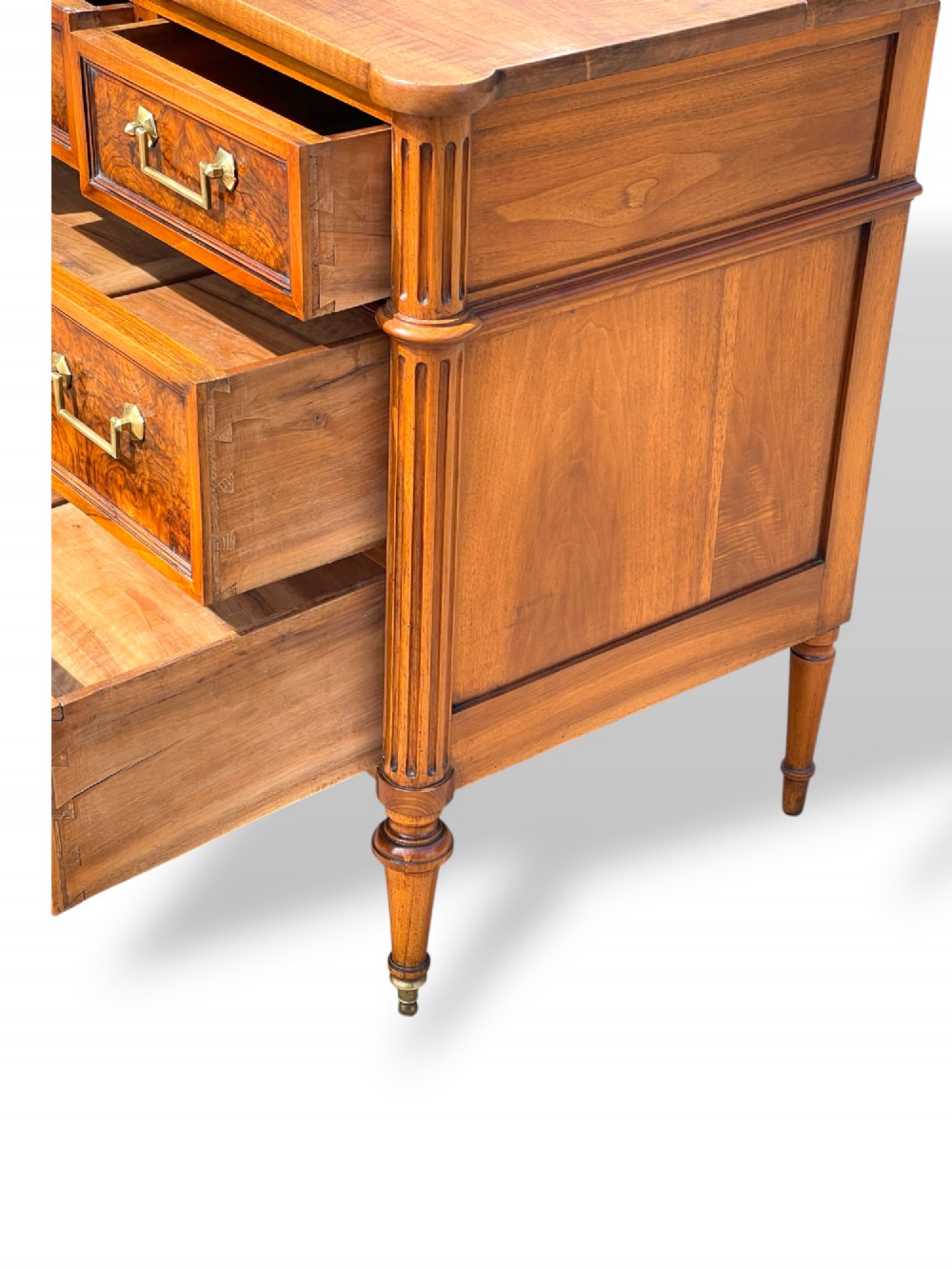 An eighteenth-century French walnut commode featuring figure-grained drawer fronts, brass handles, fluted corner pilasters, and tapered turned legs. View V
