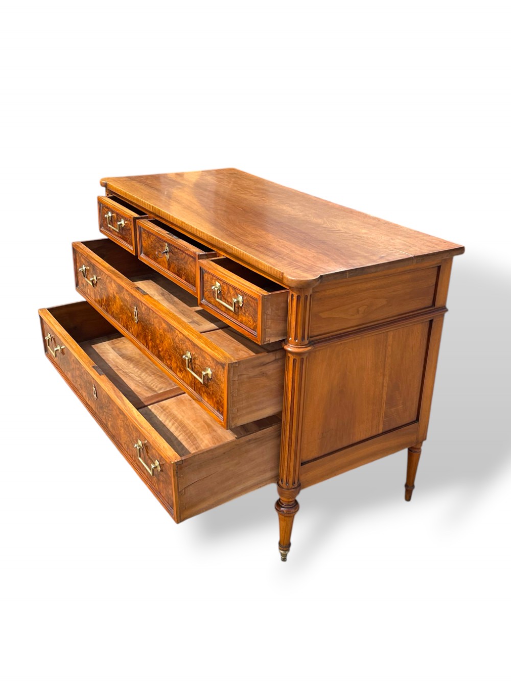 An eighteenth-century French walnut commode featuring figure-grained drawer fronts, brass handles, fluted corner pilasters, and tapered turned legs. View VI