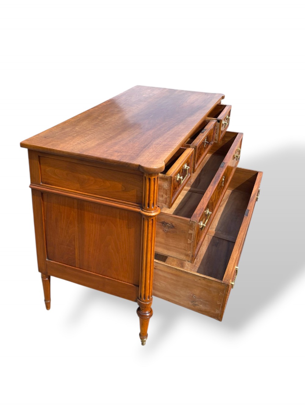 An eighteenth-century French walnut commode featuring figure-grained drawer fronts, brass handles, fluted corner pilasters, and tapered turned legs. View VII