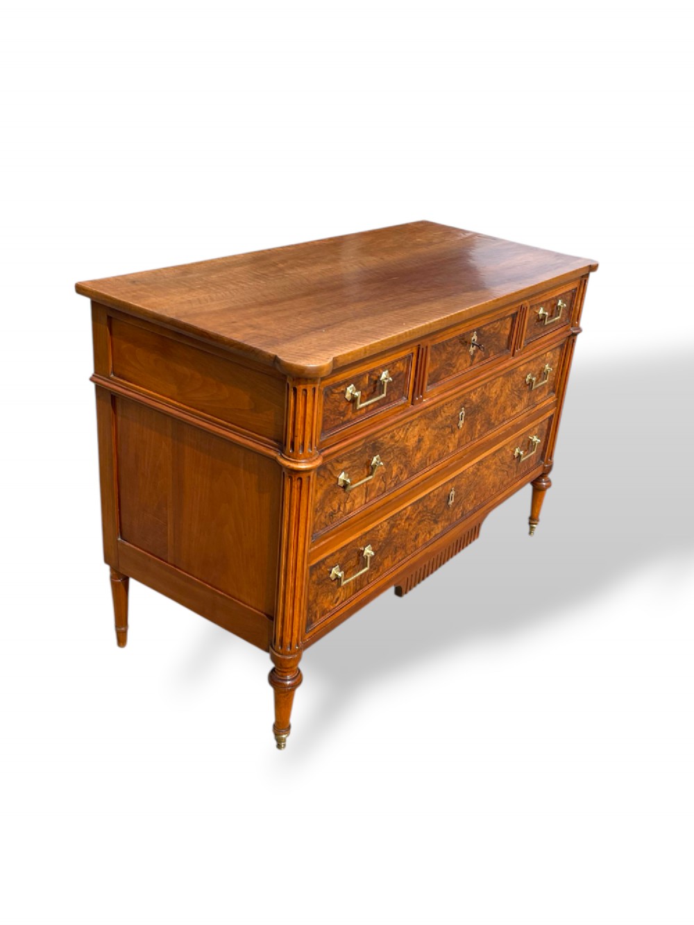An eighteenth-century French walnut commode featuring figure-grained drawer fronts, brass handles, fluted corner pilasters, and tapered turned legs. View IX
