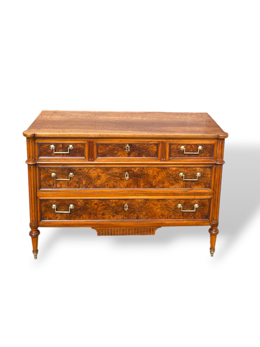 An eighteenth-century French walnut commode featuring figure-grained drawer fronts, brass handles, fluted corner pilasters, and tapered turned legs. View X