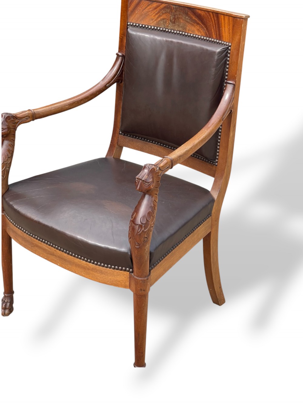A pair of twentieth-century French Empire style armchairs featuring carved mahogany frames, dark brown leather upholstery, and brass stud trim. View V