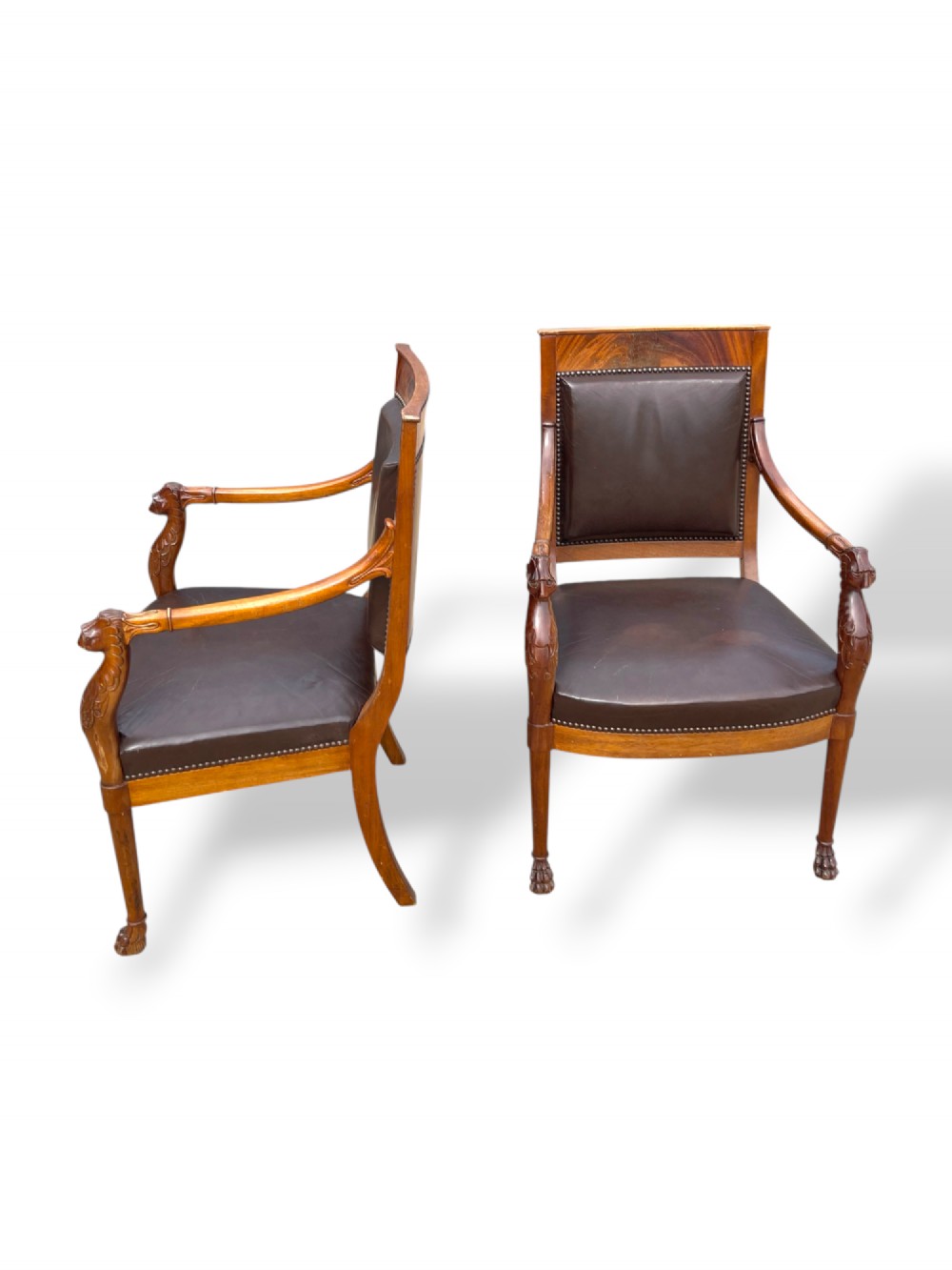 A pair of twentieth-century French Empire style armchairs featuring carved mahogany frames, dark brown leather upholstery, and brass stud trim. View X