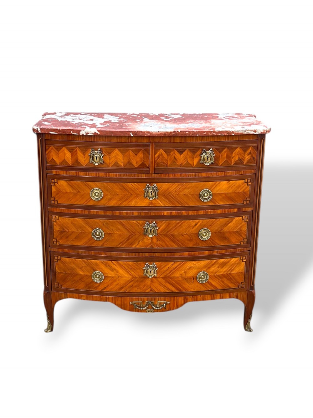A 19th-century French wooden commode featuring chevron parquetry veneer, decorative brass handles, keyhole mounts, and a variegated reddish-pink marble top.