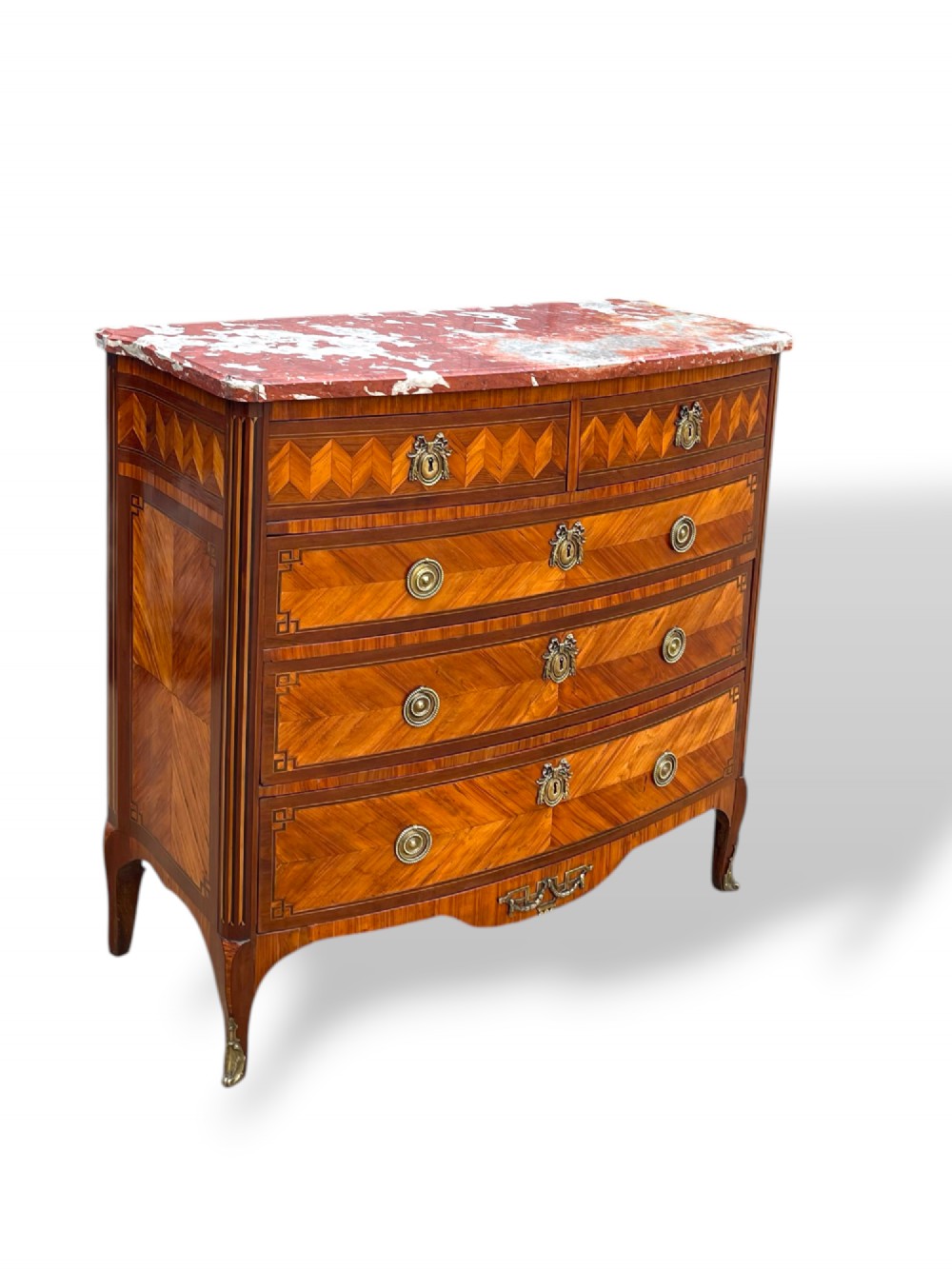 A 19th-century French wooden commode featuring chevron parquetry veneer, decorative brass handles, keyhole mounts, and a variegated reddish-pink marble top. View V