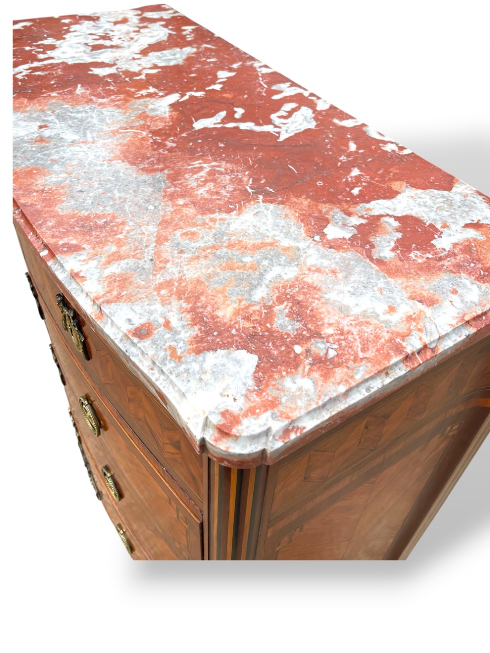 A 19th-century French wooden commode featuring chevron parquetry veneer, decorative brass handles, keyhole mounts, and a variegated reddish-pink marble top. View VI