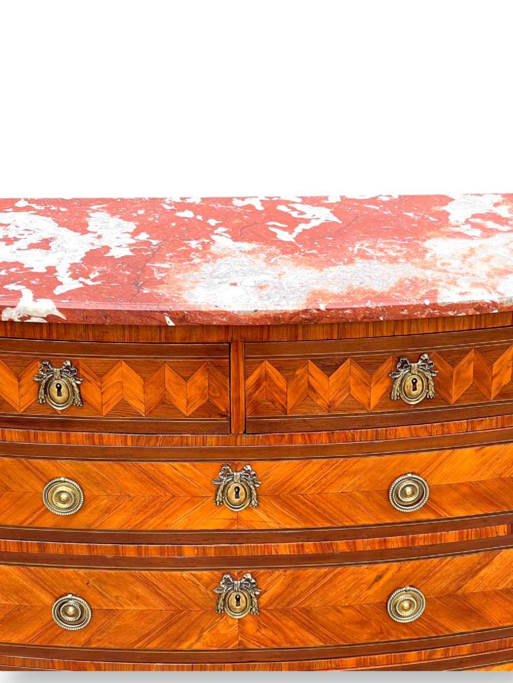 A 19th-century French wooden commode featuring chevron parquetry veneer, decorative brass handles, keyhole mounts, and a variegated reddish-pink marble top. View VII