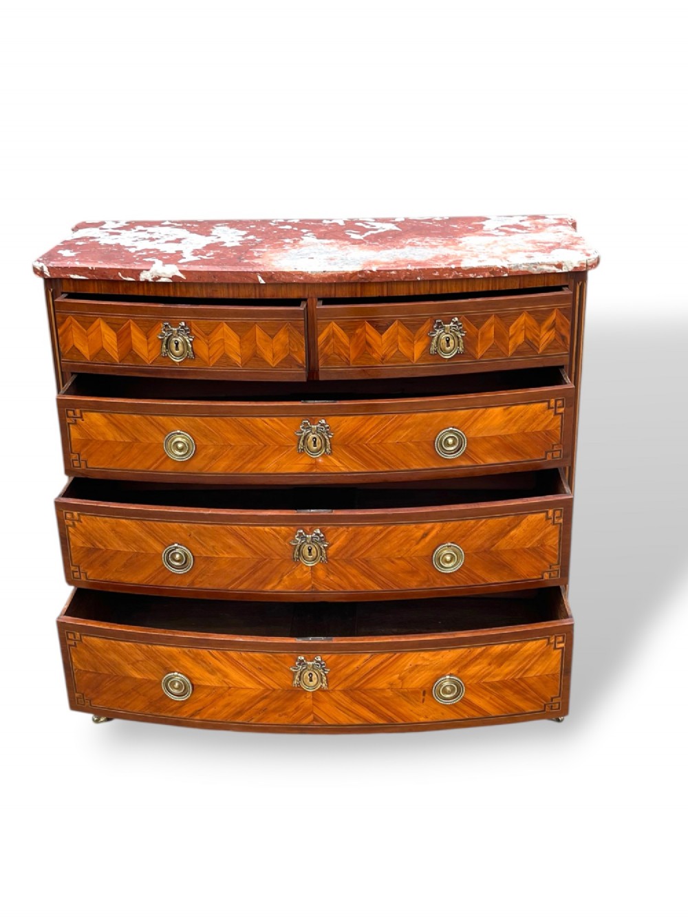 A 19th-century French wooden commode featuring chevron parquetry veneer, decorative brass handles, keyhole mounts, and a variegated reddish-pink marble top. View X