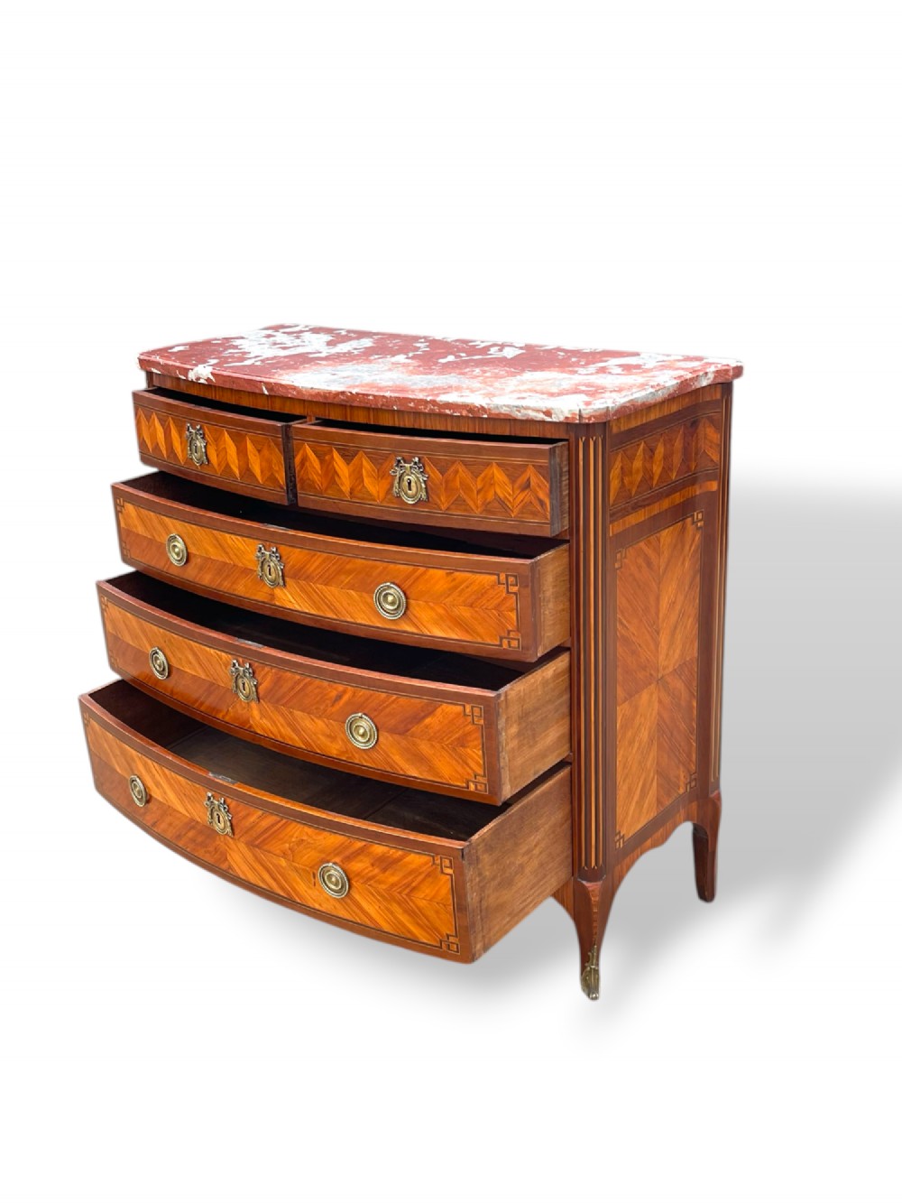 A 19th-century French wooden commode featuring chevron parquetry veneer, decorative brass handles, keyhole mounts, and a variegated reddish-pink marble top. View XI