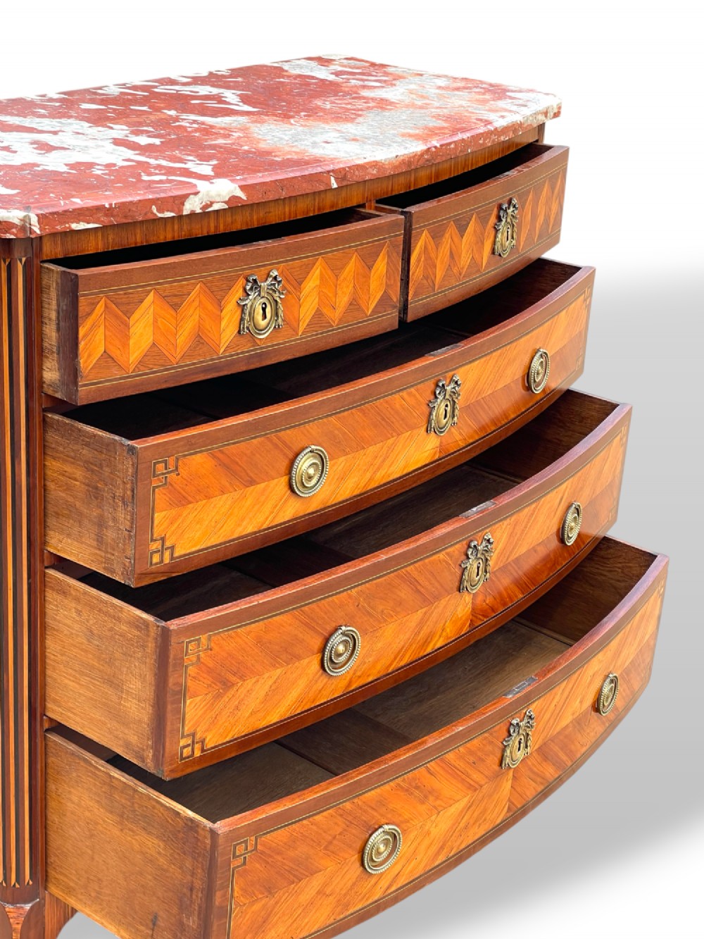 A 19th-century French wooden commode featuring chevron parquetry veneer, decorative brass handles, keyhole mounts, and a variegated reddish-pink marble top. View XIII