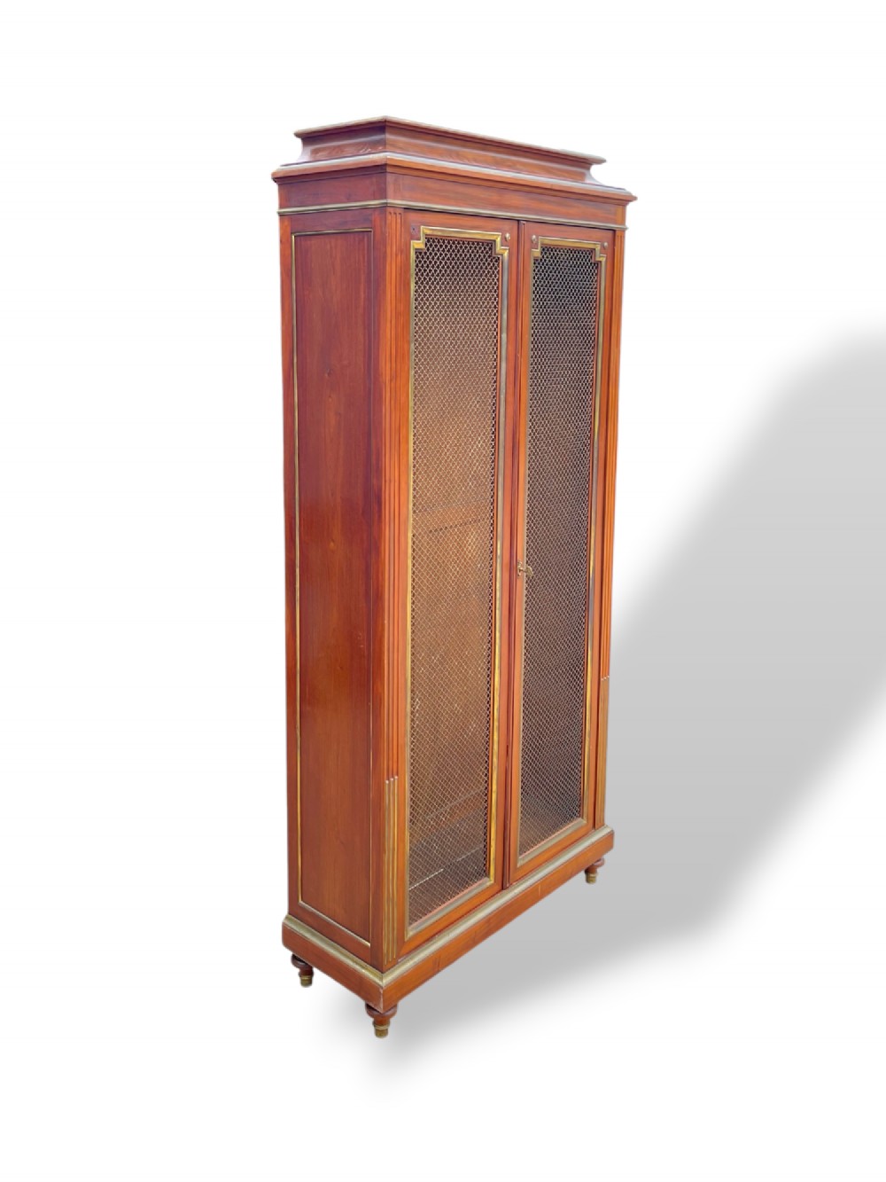 A tall French Empire style mahogany two-door bookcase featuring brass wire mesh door panels and fluted side columns. View IX