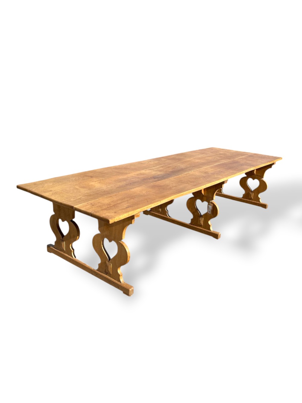 A large 19th-century English oak low coffee table featuring a three-plank top and trestle legs with heart-shaped cutouts connected by a central stretcher.