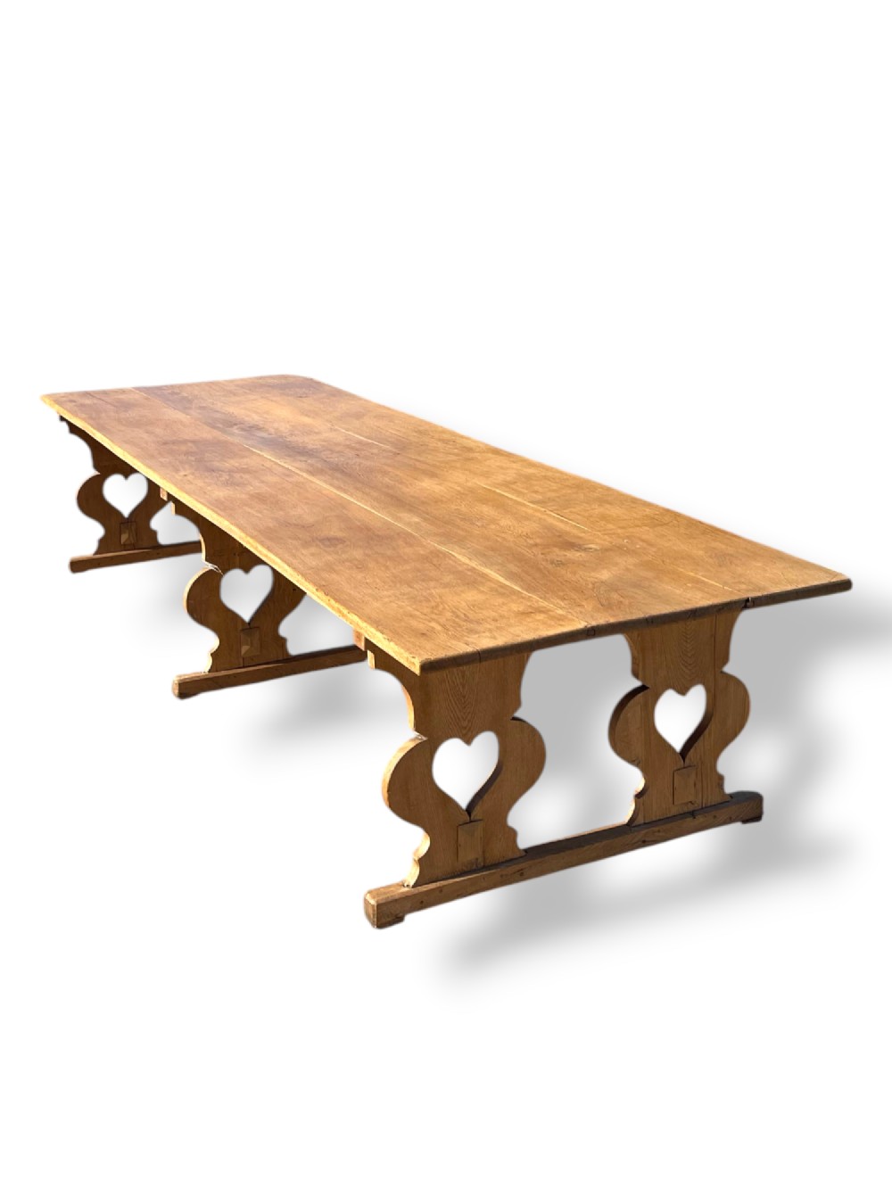 A large 19th-century English oak low coffee table featuring a three-plank top and trestle legs with heart-shaped cutouts connected by a central stretcher. View V