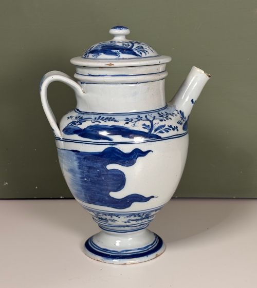 fig 1. An 18th-century blue and white tin-glazed Delftware spouted apothecary jar featuring a fitted lid, side handle, and painted foliate decoration.