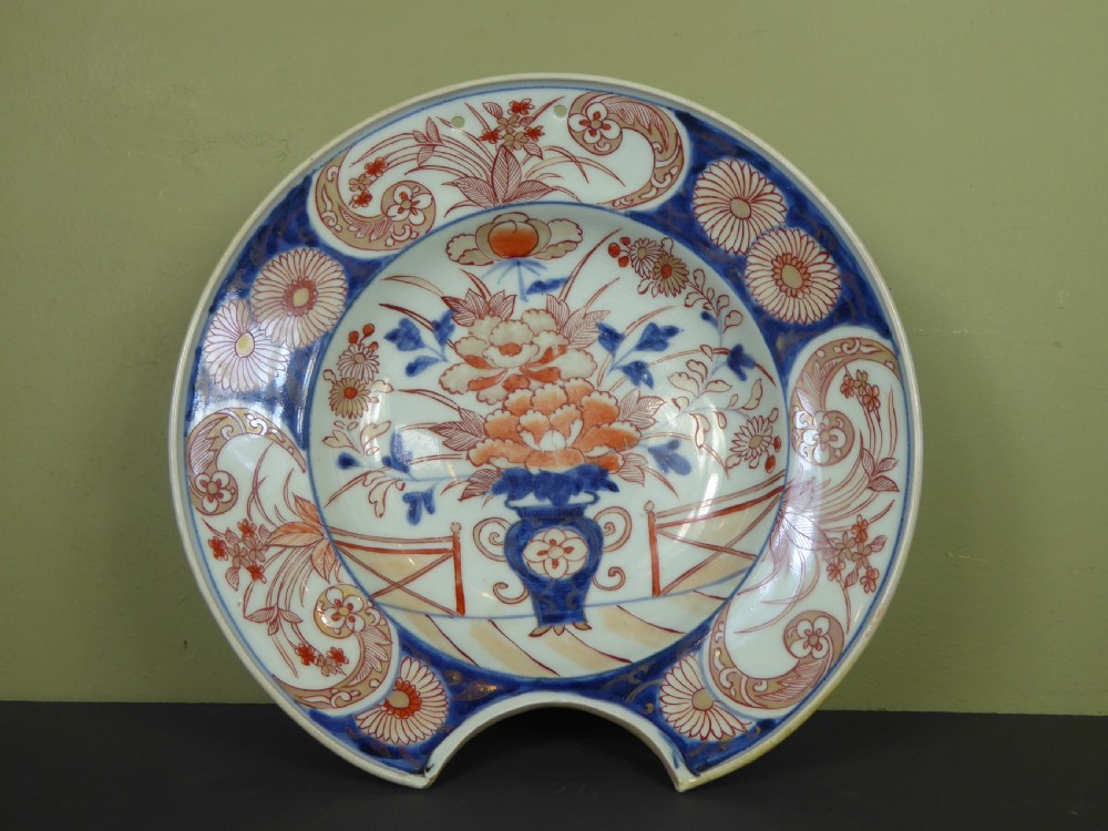 An 18th-century Imari porcelain shaving bowl decorated with hand-painted blue and iron-red floral motifs, featuring a crescent cut-out along the rim. View III