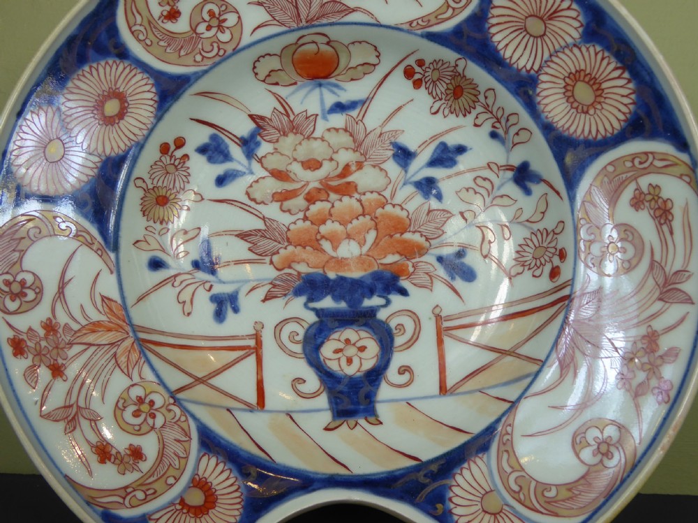 An 18th-century Imari porcelain shaving bowl decorated with hand-painted blue and iron-red floral motifs, featuring a crescent cut-out along the rim. View V