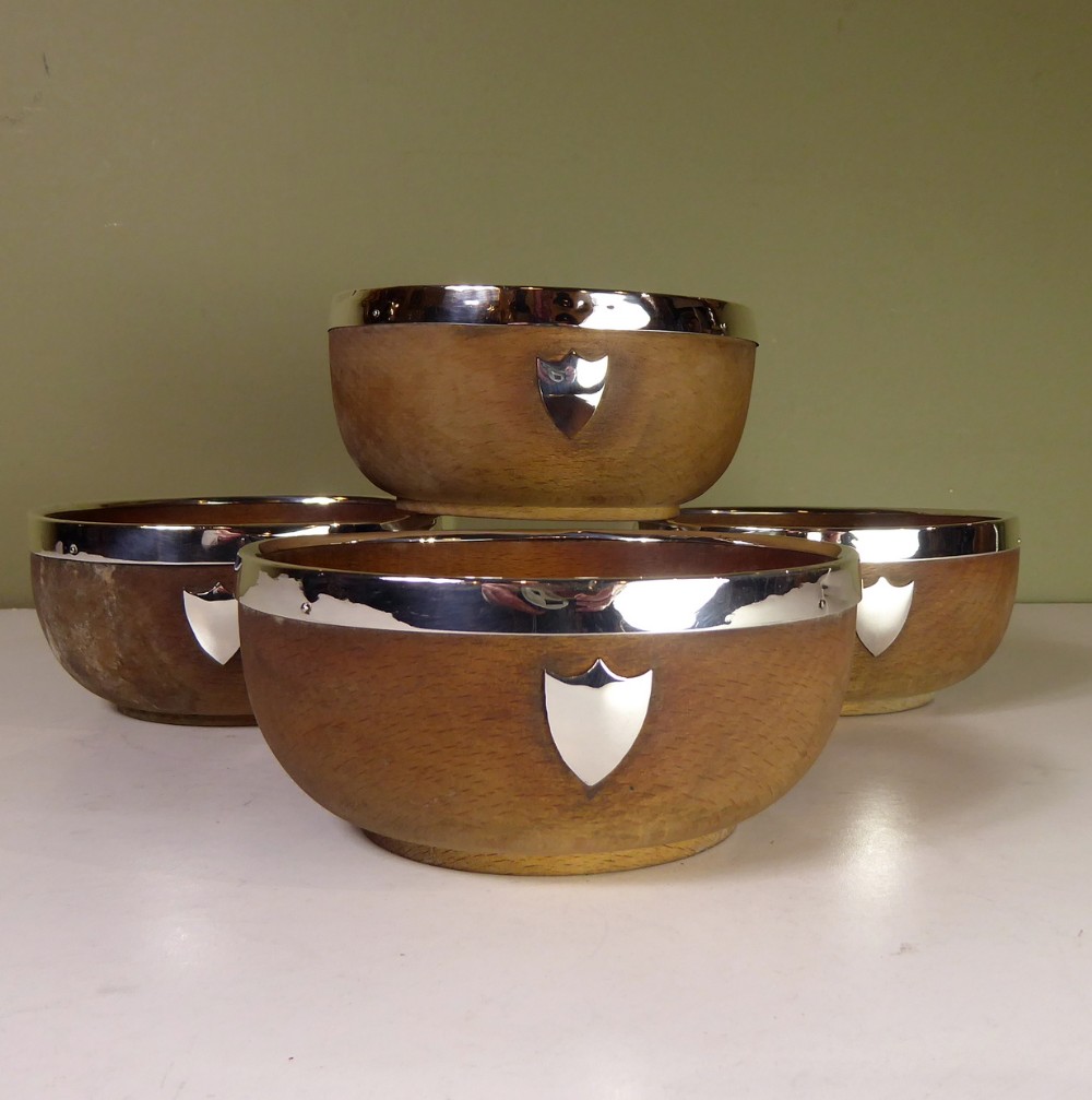 A set of four turned oak wooden bowls featuring polished silver rim bands and blank silver shield crests on the front.
