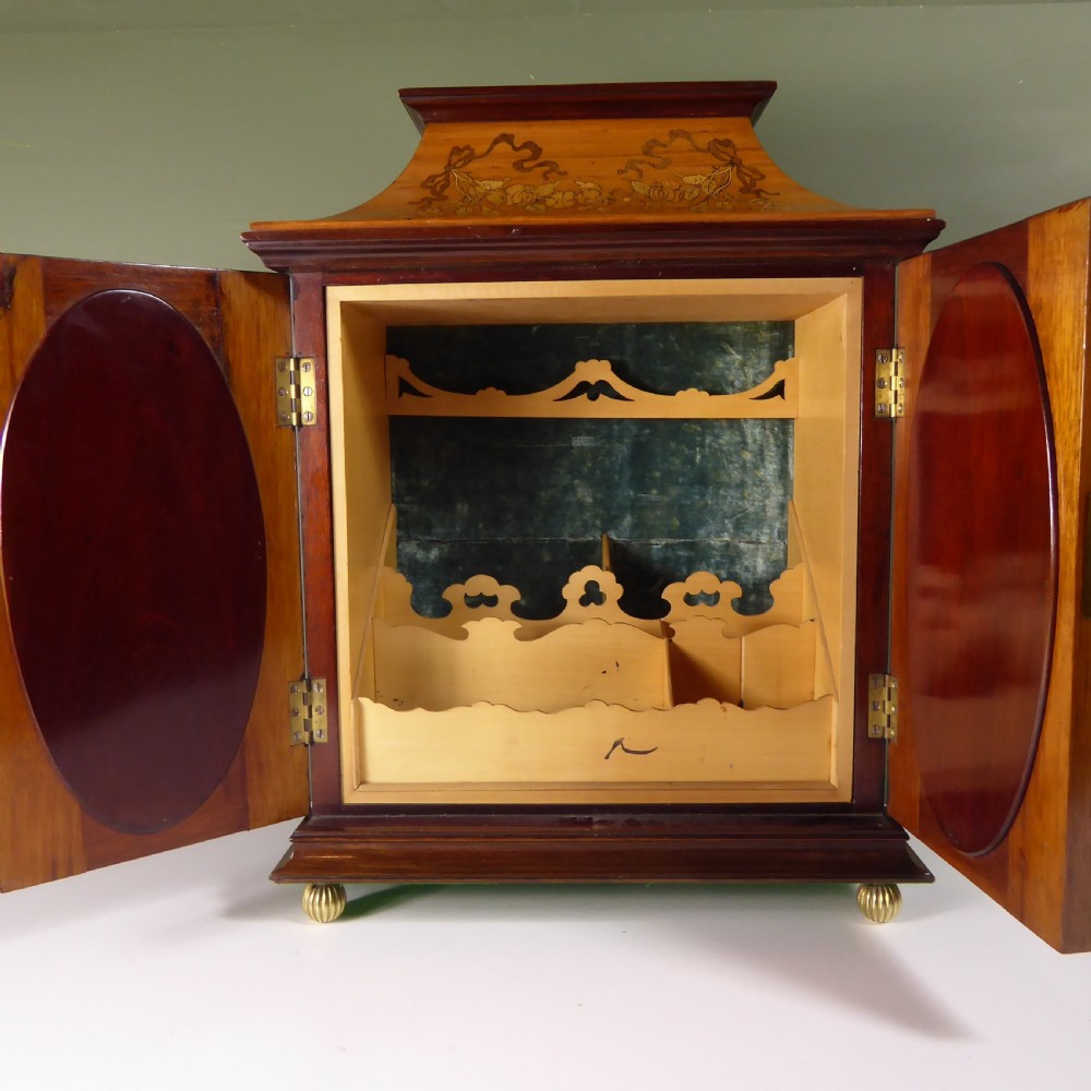 A 19th-century wooden tabletop cabinet featuring oval mirrored double doors, brass handles, brass ball feet, and floral marquetry inlay. View II