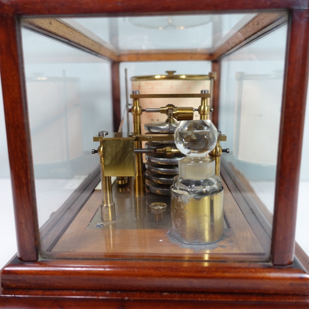 An antique mahogany cased barograph featuring a brass recording mechanism and drum enclosed within a glazed glass display case with a lower drawer. View VI