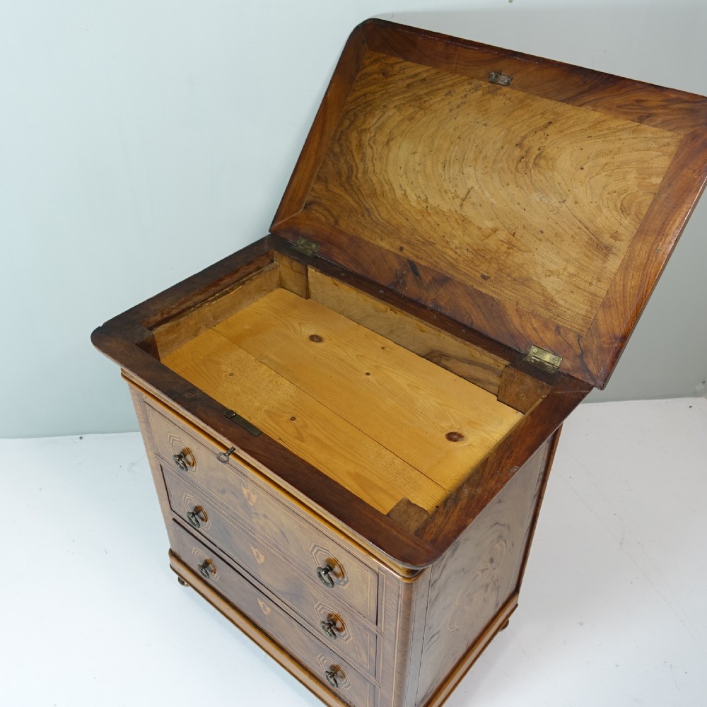 A 19th-century miniature wooden chest of drawers featuring three inlaid drawers, octagonal ring handles, shield escutcheons, and small turned feet. View IV