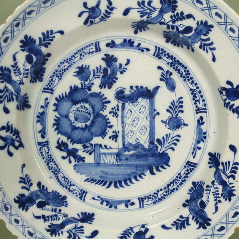 An 18th-century circular tin-glazed earthenware charger featuring hand-painted cobalt blue floral motifs and a crosshatch patterned rim on a white background. View II