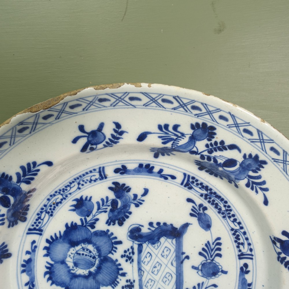 An 18th-century circular tin-glazed earthenware charger featuring hand-painted cobalt blue floral motifs and a crosshatch patterned rim on a white background. View IV