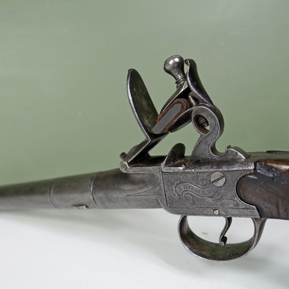 An 18th-century steel box-lock flintlock pistol featuring an engraved lockplate, steel trigger guard, and polished dark walnut grip. View II