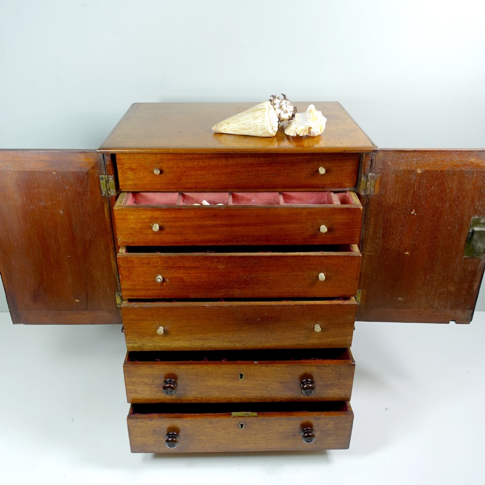 An early 19th-century mahogany miniature cabinet featuring twin upper cupboard doors, two lower drawers with turned knobs, and small ball feet. View II
