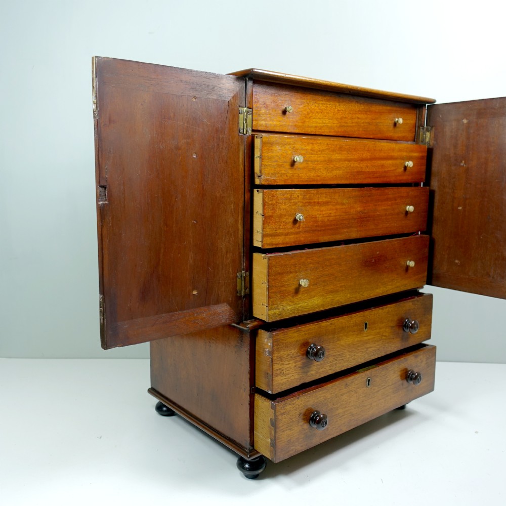 An early 19th-century mahogany miniature cabinet featuring twin upper cupboard doors, two lower drawers with turned knobs, and small ball feet. View III