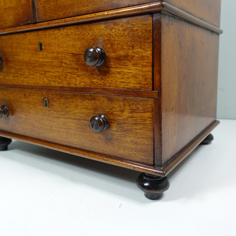 An early 19th-century mahogany miniature cabinet featuring twin upper cupboard doors, two lower drawers with turned knobs, and small ball feet. View VI