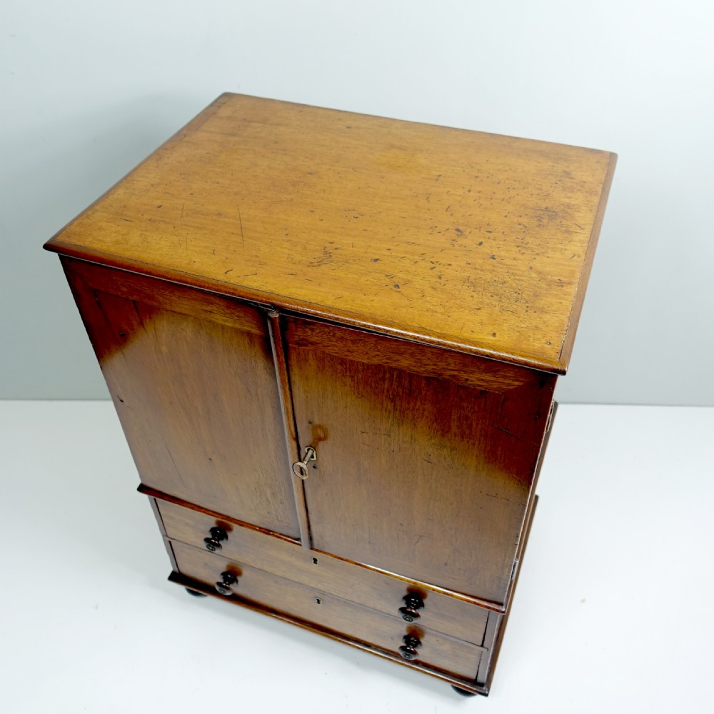 An early 19th-century mahogany miniature cabinet featuring twin upper cupboard doors, two lower drawers with turned knobs, and small ball feet. View VII