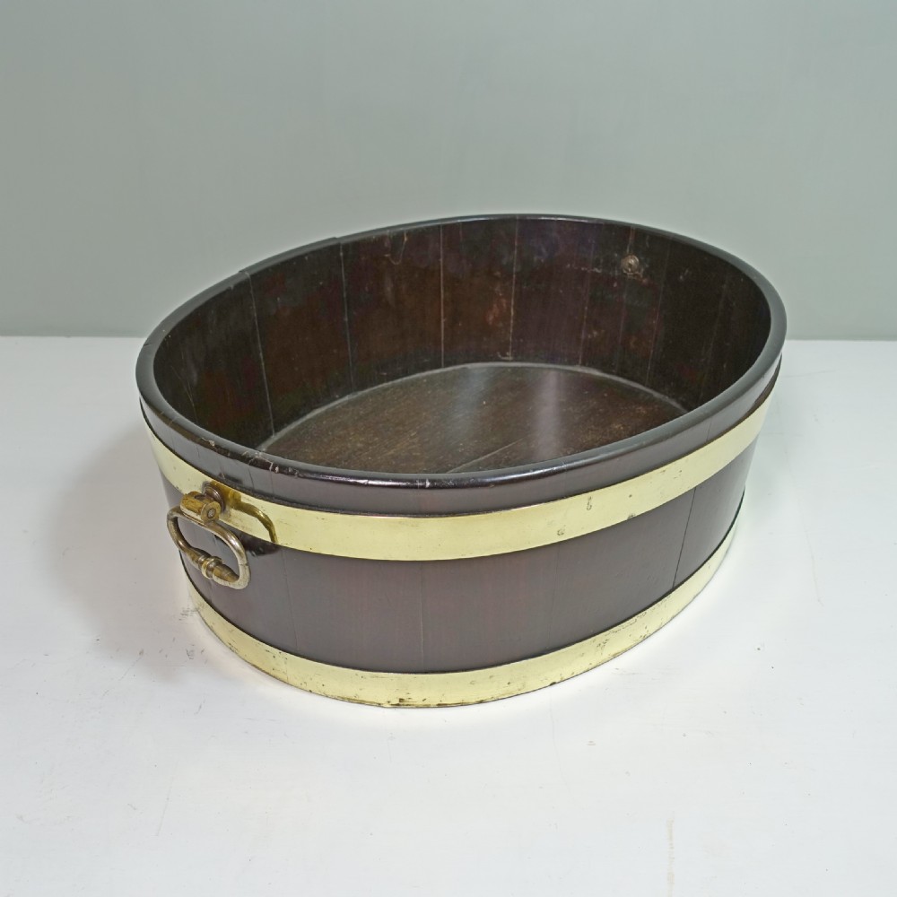 An 18th-century oval mahogany wine cooler featuring coopered wooden staves held together by two wide brass bands and fitted with side brass handles.
