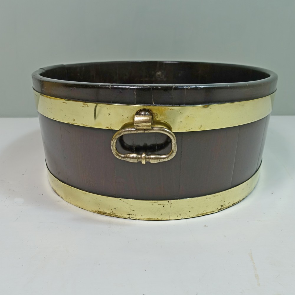 An 18th-century oval mahogany wine cooler featuring coopered wooden staves held together by two wide brass bands and fitted with side brass handles. View VI
