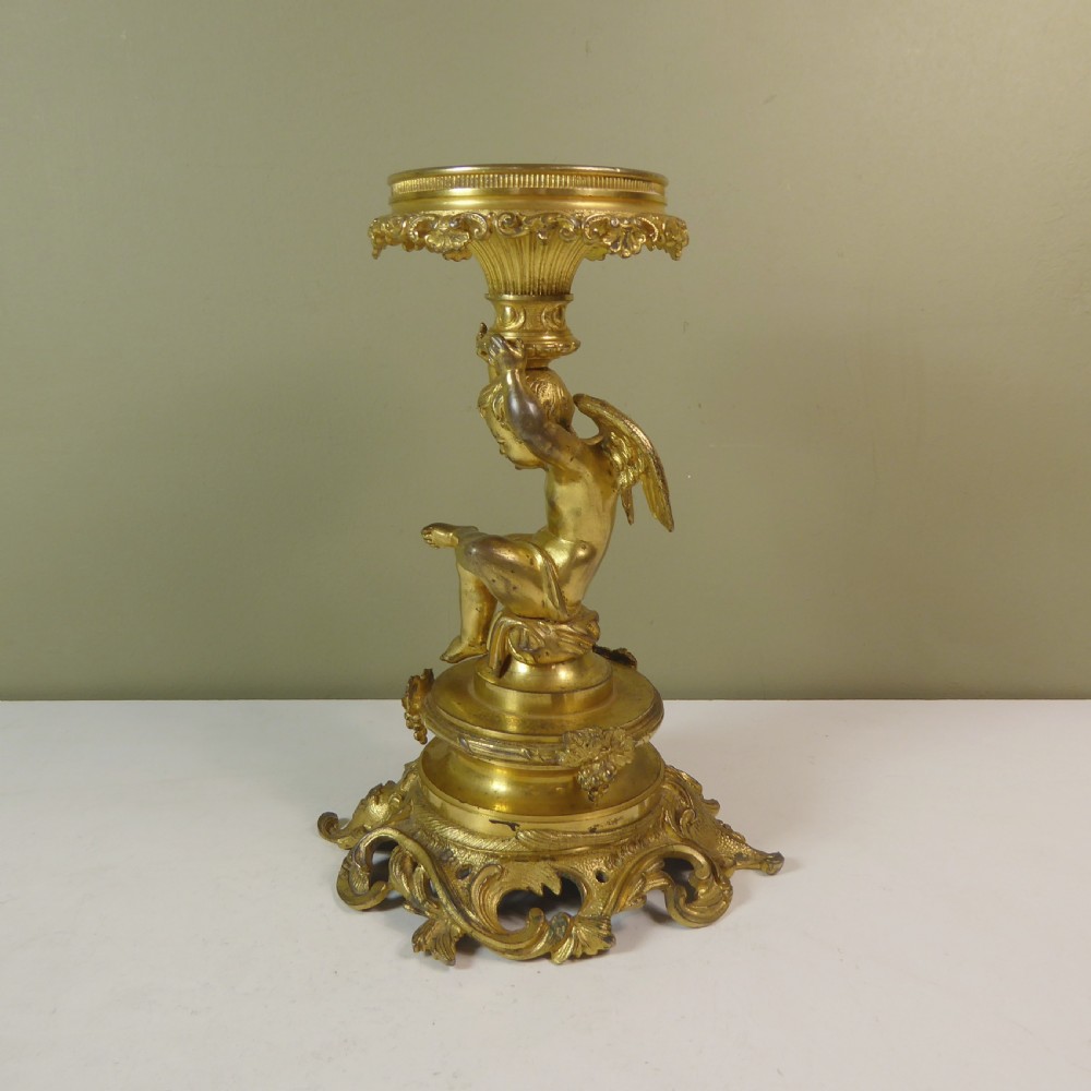 A 19th-century gilt bronze ormolu tazza base featuring a winged cherub figure supporting a fluted capital above a rococo scrolled pedestal.