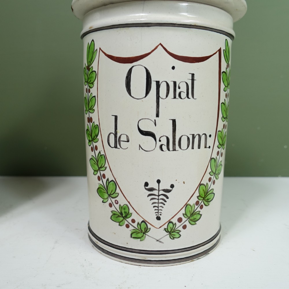 A pair of 18th-century tin-glazed ceramic apothecary jars with off-white bodies, hand-painted green laurel wreaths, black pharmaceutical inscriptions, and conical lids with green finials. View VIII