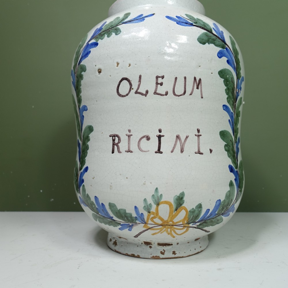 An 18th-century tin-glazed earthenware apothecary jar in off-white, hand-painted with green leaves, a yellow ribbon bow, and Latin text. View III