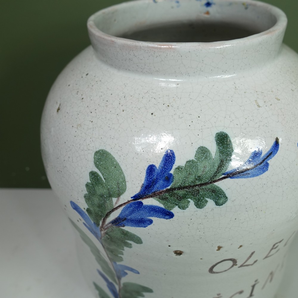 An 18th-century tin-glazed earthenware apothecary jar in off-white, hand-painted with green leaves, a yellow ribbon bow, and Latin text. View IX