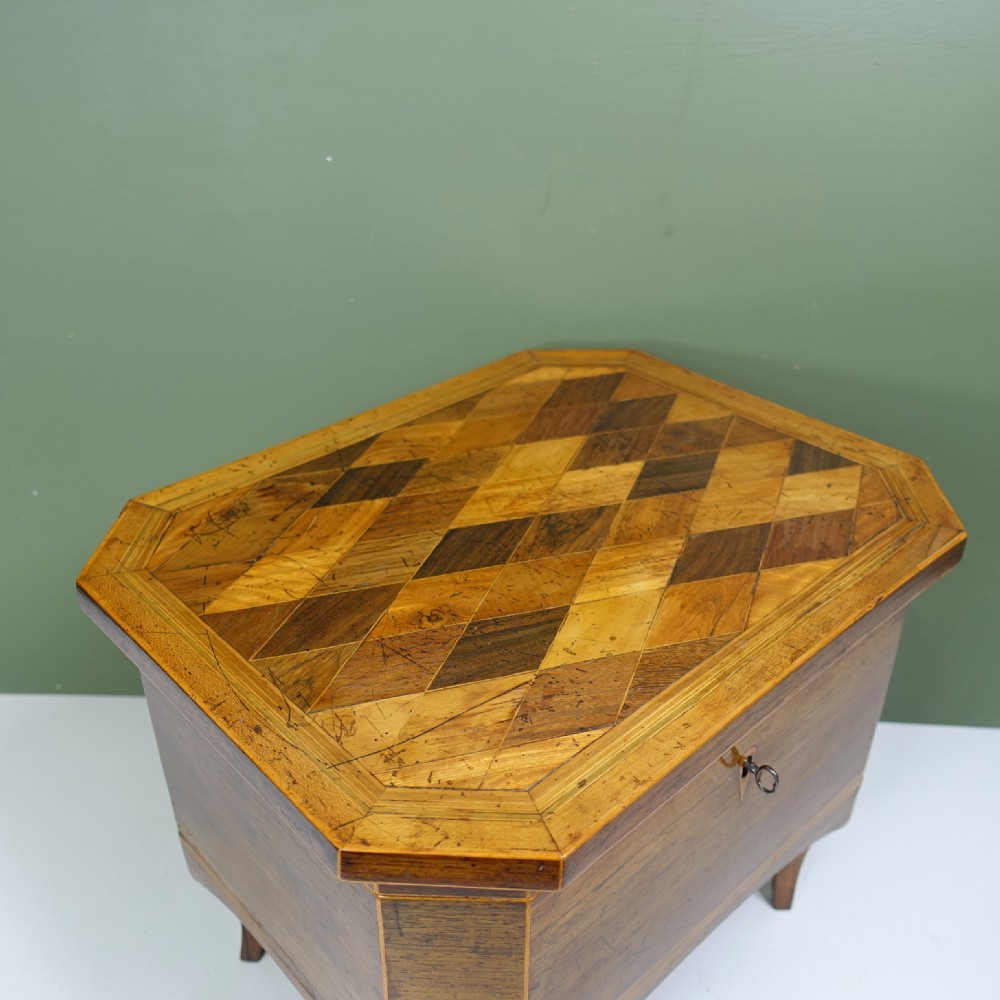 An early nineteenth-century wooden caddy featuring geometric parquetry inlay on the lid, canted corners, crossbanded sides, and integrated tapered legs. View III